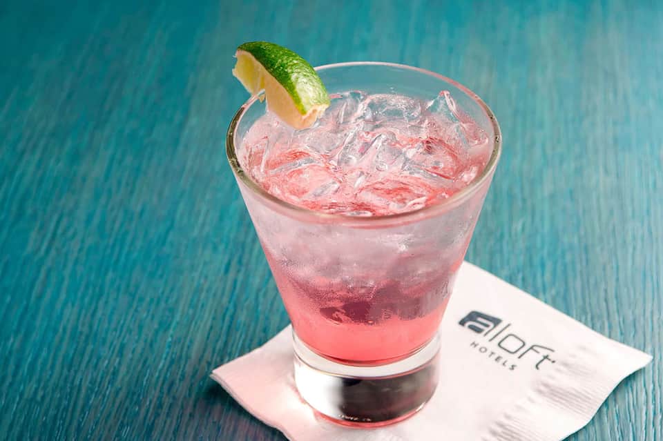 Pink cocktail with lime wedge on turquoise table surface near poolside at aloft hotel