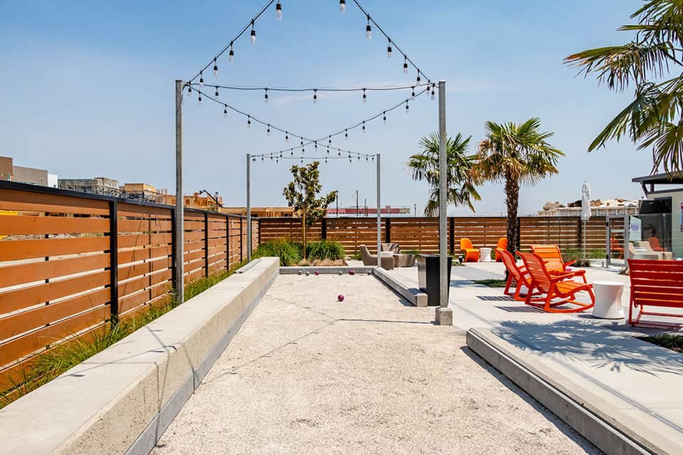 Rooftop deck with string lights, red adirondack chairs, wooden fence, and city views