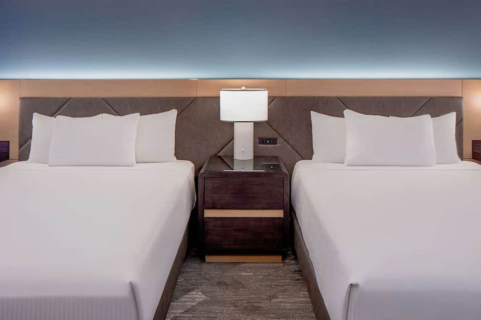 Upscale hotel room with two queen beds, dark headboards, and modern bedding