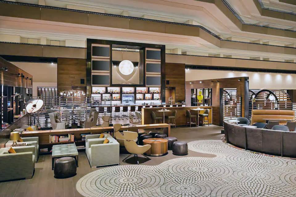 Contemporary hotel lobby with modern bar, geometric patterned carpet, and brown wood accents