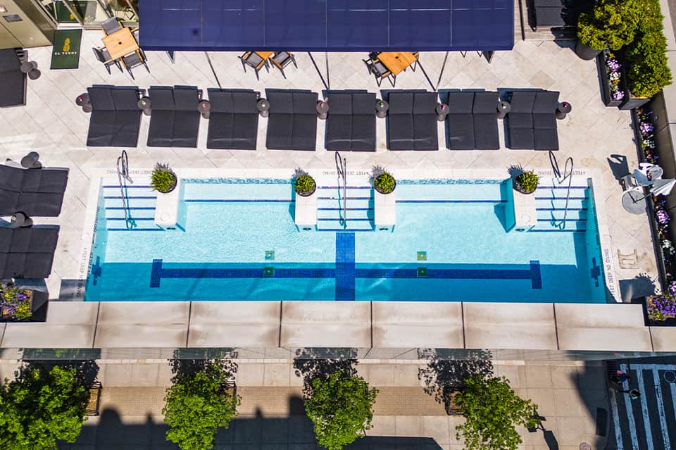 Overhead view of rectangular lap pool with black loungers and blue umbrellas on concrete deck