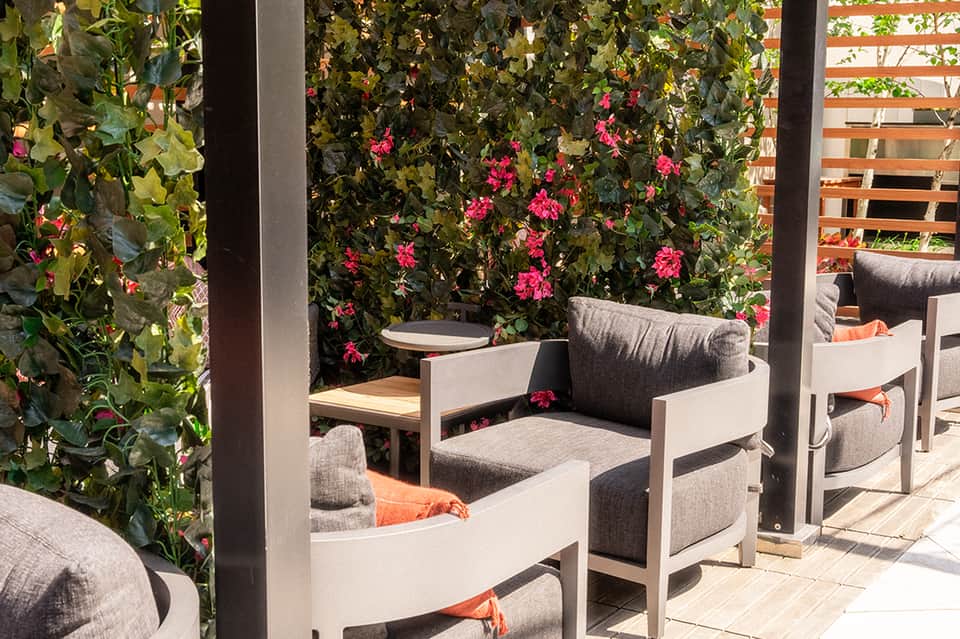 Garden seating area with white chairs, dark cushions, flowering vines, and brick wall backdrop