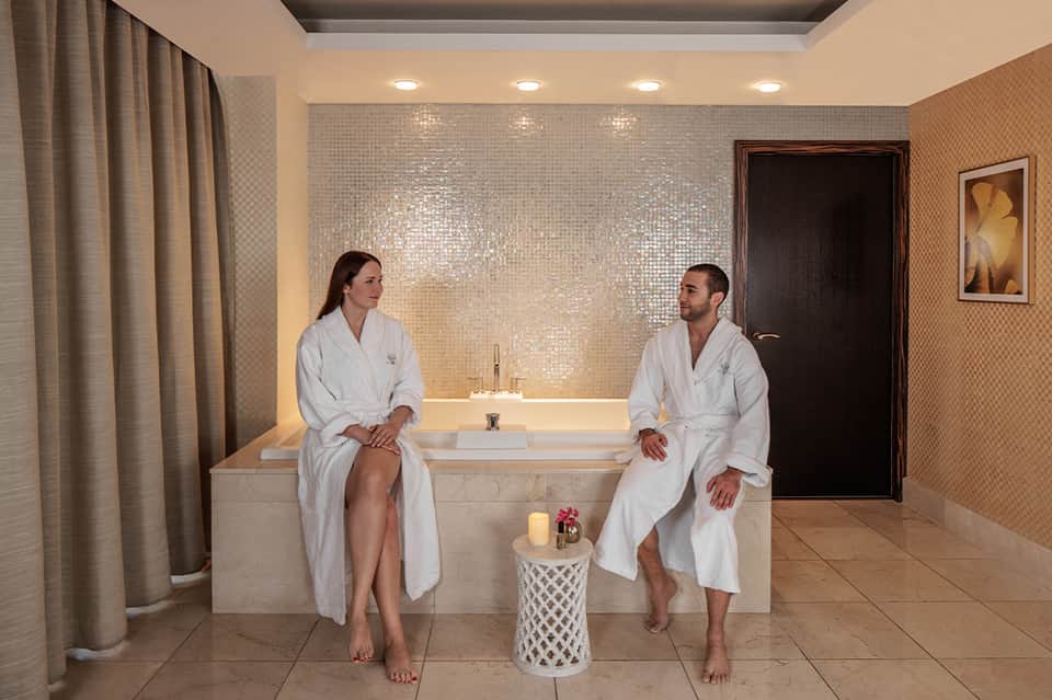 Spa relaxation area with two people in white robes sitting by a luxurious soaking tub