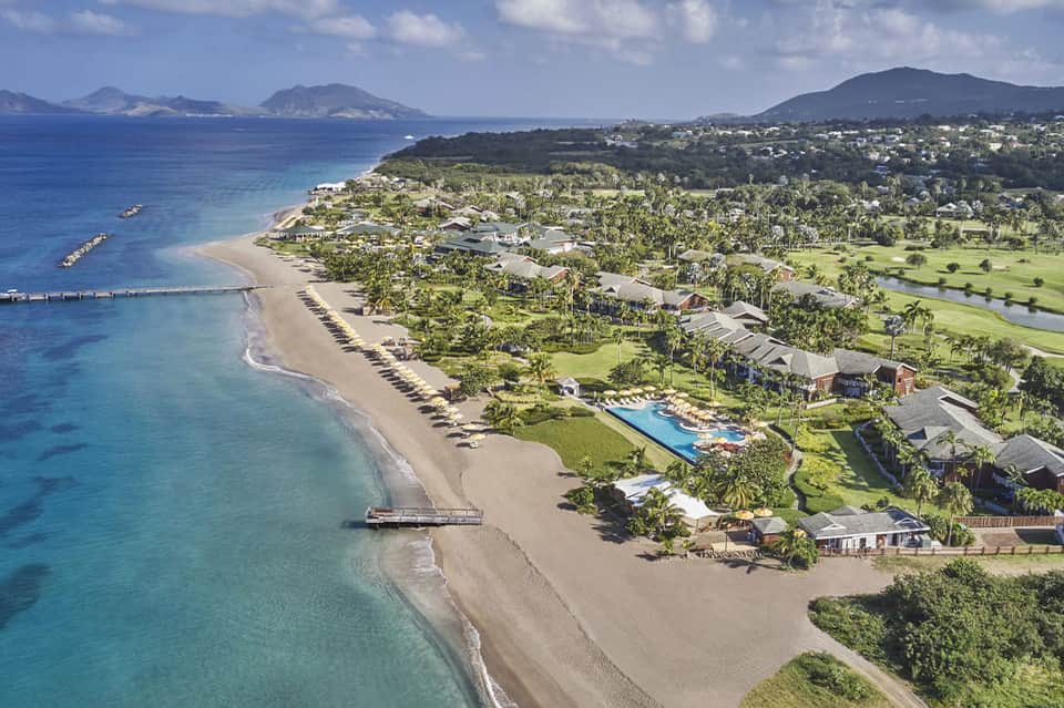 Aerial view of beachfront resort with pool, sand beach, palm trees, and surrounding tropical landscape