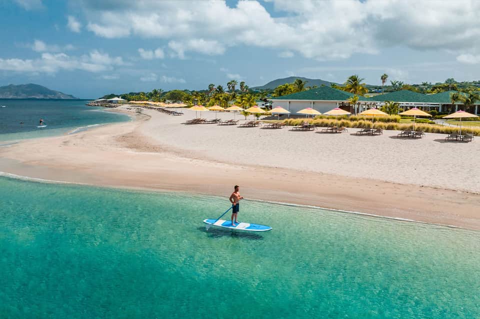Guest paddleboarding in turquoise water off pristine white sand beach with umbrellas