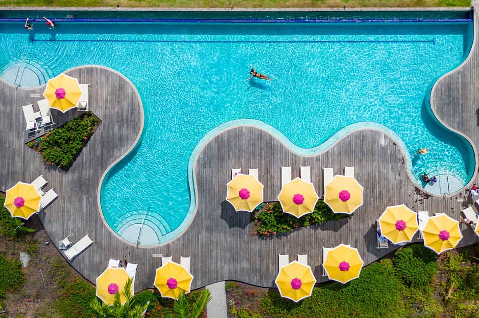 Overhead view of resort pool with blue water, yellow umbrellas, and curved deck design