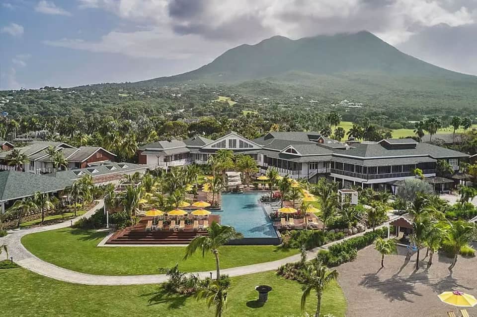 Luxury resort with pool, lush landscaping, yellow umbrellas, and volcano mountain backdrop