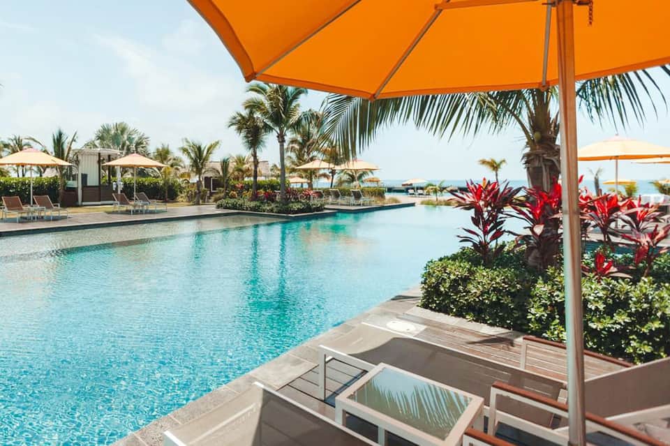 Resort lagoon pool with orange umbrellas, palm trees, and tropical landscaping