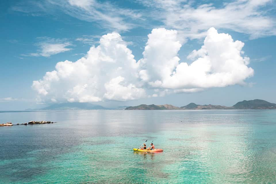Crystal clear turquoise water with kayakers, mountains, and white clouds