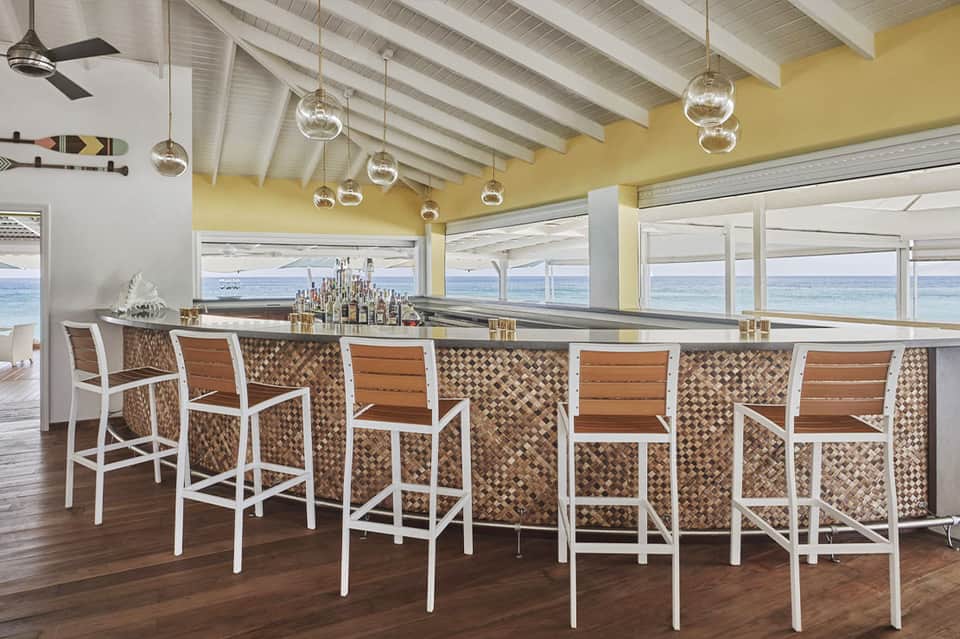 Beachfront bar with ocean views, yellow ceiling, pendant lighting, and patterned bar stools