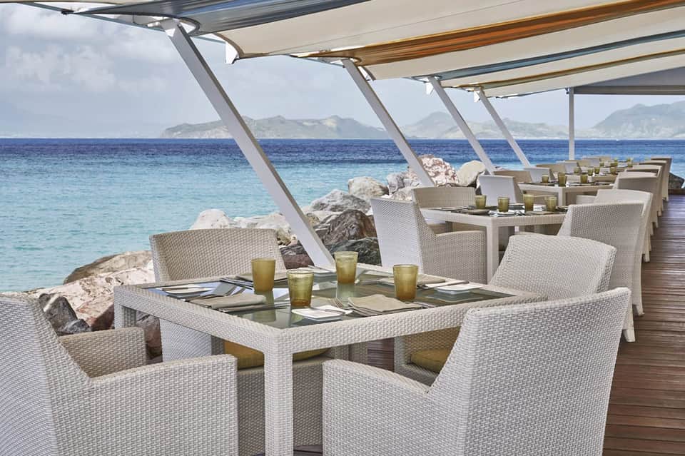 Waterfront dining pavilion with white furniture overlooking Mediterranean sea and rocky coastline