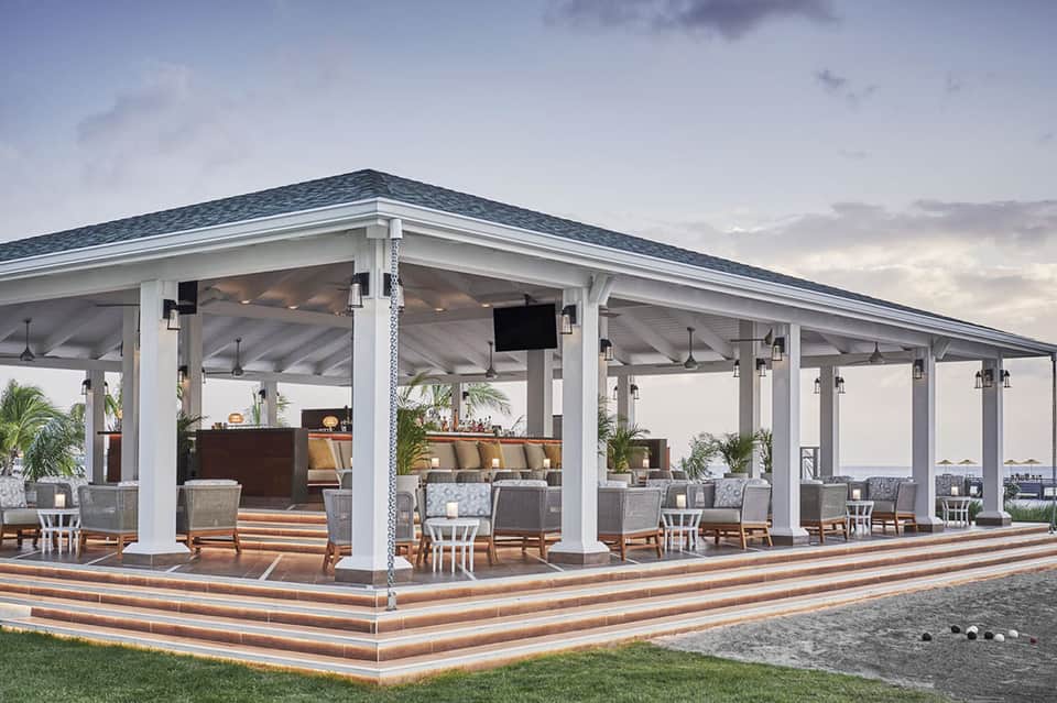 Covered oceanfront pavilion with white columns, dark roof, lounge seating, and water views