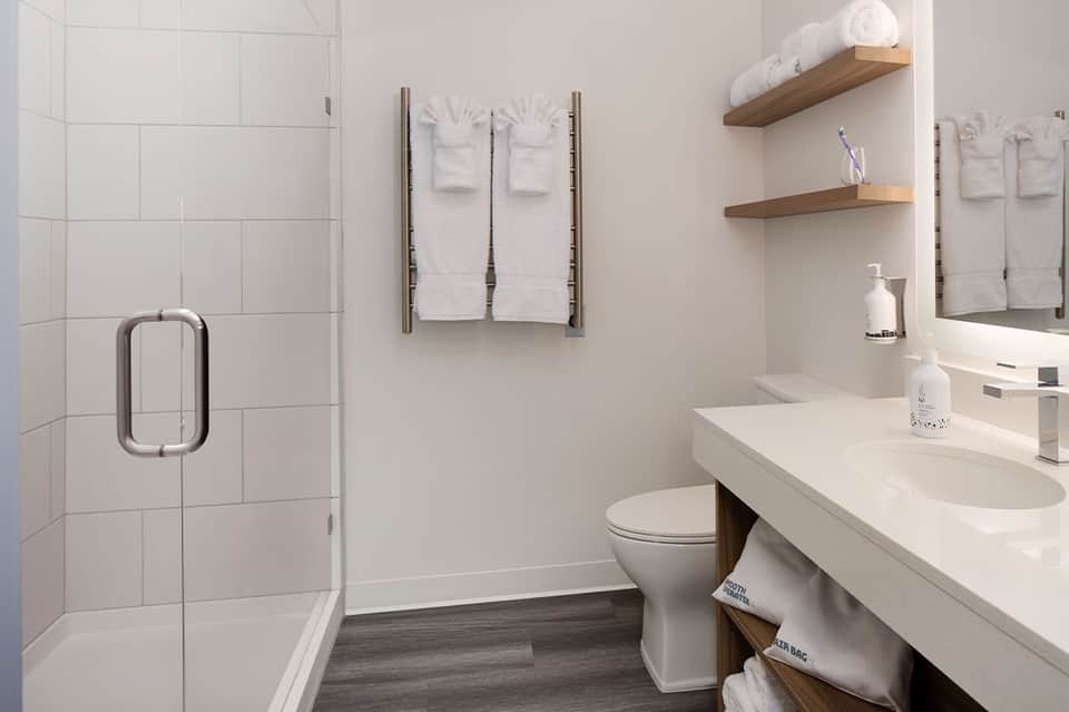 Modern bathroom with white tile shower, floating shelves, and clean countertop vanity