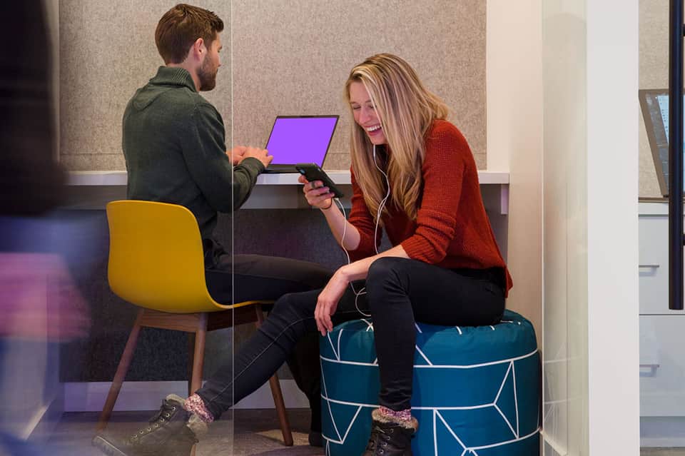 Two people collaborating in a modern hotel workspace with geometric pouf seating