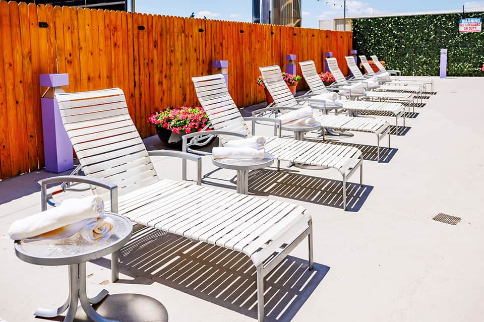 Row of white lounge chairs along an orange wood fence at a hotel pool deck with flowers