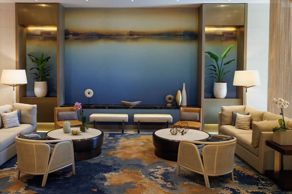 Modern hotel lounge with curved seating, marble fireplace, artwork, and neutral earth tones