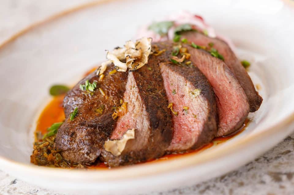 Beautifully plated medium-rare duck breast with herb garnish on white plate