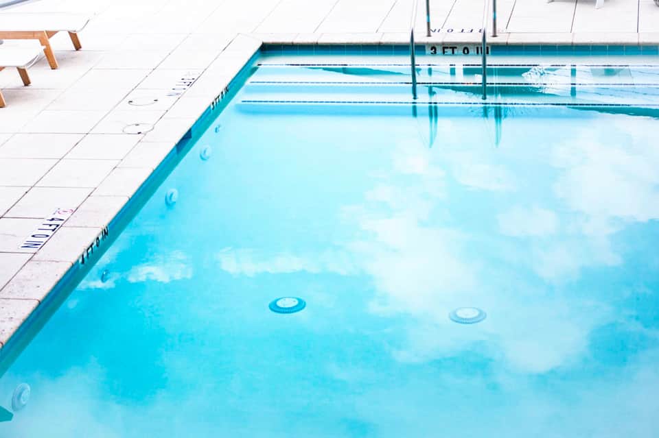 Olympic-sized swimming pool with lane markings, clear turquoise water, and white deck area with lounge chairs