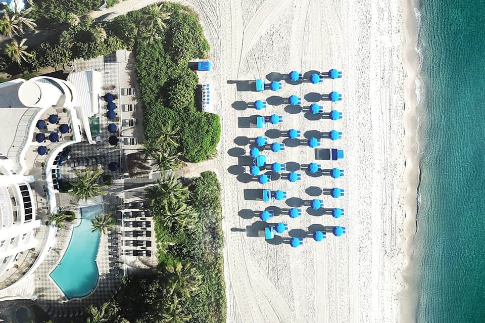 Aerial view of beachfront resort with pool, sun umbrellas, and pristine white sand beach