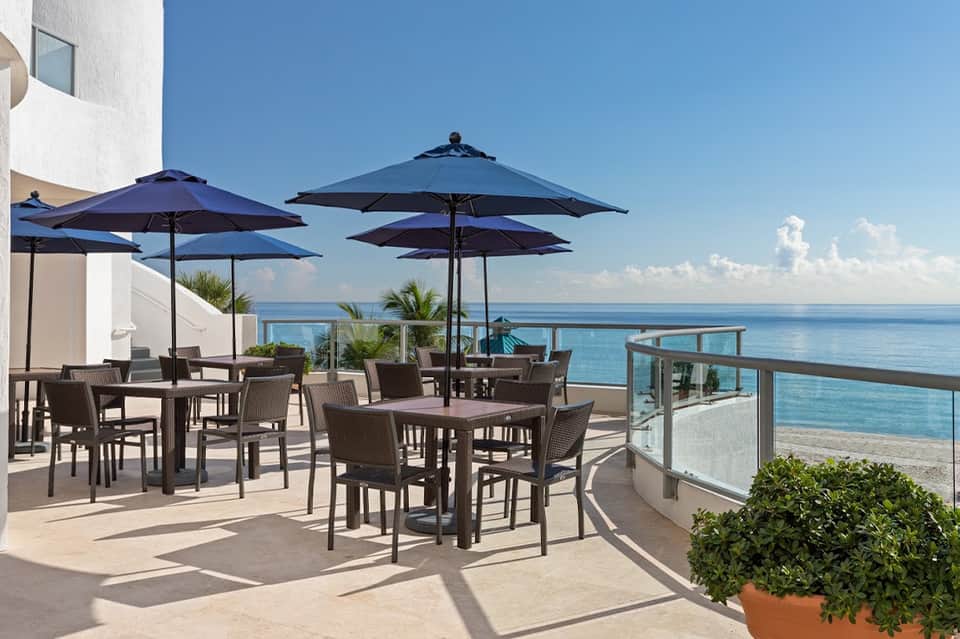 Beachfront terrace with dark umbrellas, dining tables, and ocean views from modern resort balcony