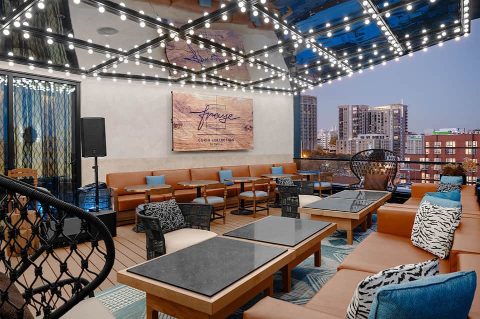 Rooftop lounge with orange seating, string lights, and city skyline views at evening