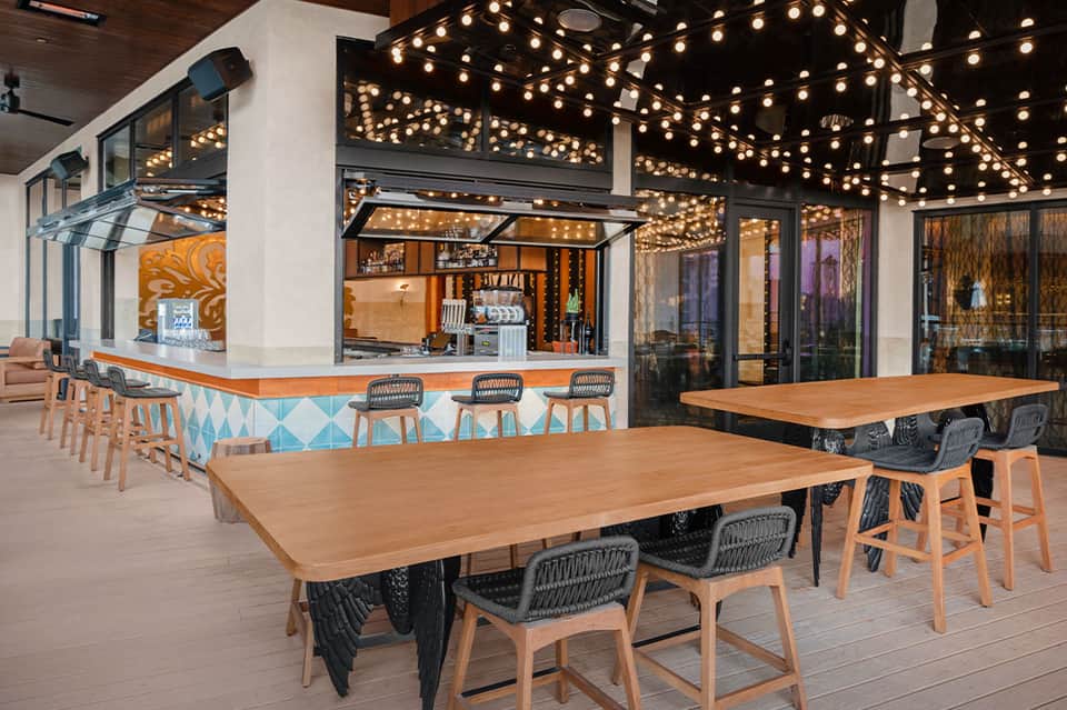 Modern outdoor dining area with wooden tables, decorative lighting, and ocean-view bar