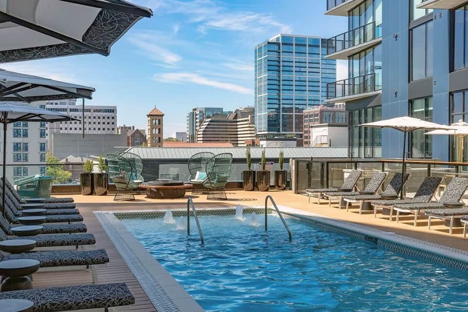 Urban rooftop pool deck with lounge chairs, umbrellas, and city skyline views