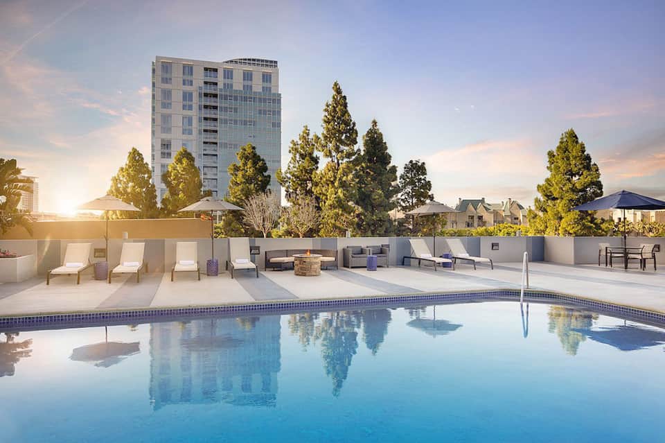Modern rooftop pool with white lounge chairs, fire pit, and city views at dusk