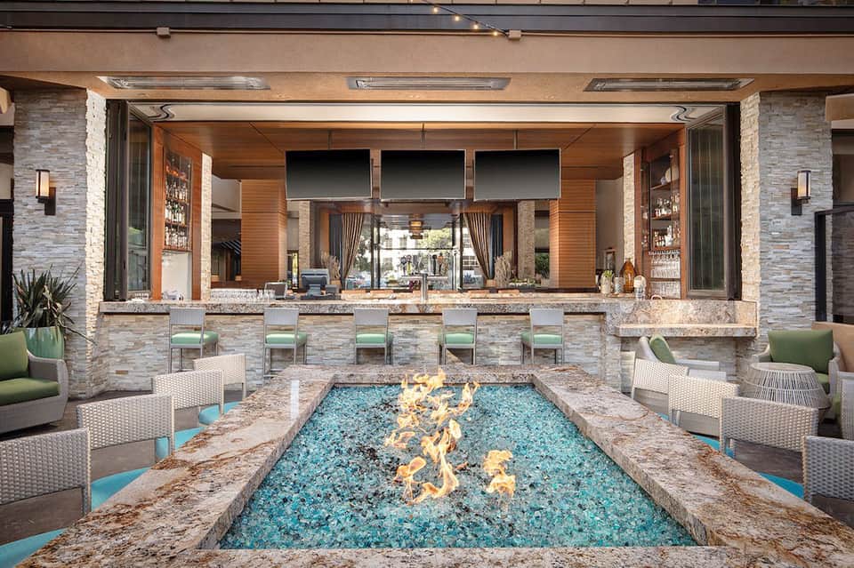 Modern outdoor bar with stone fireplace, turquoise fire feature, and lounge seating area