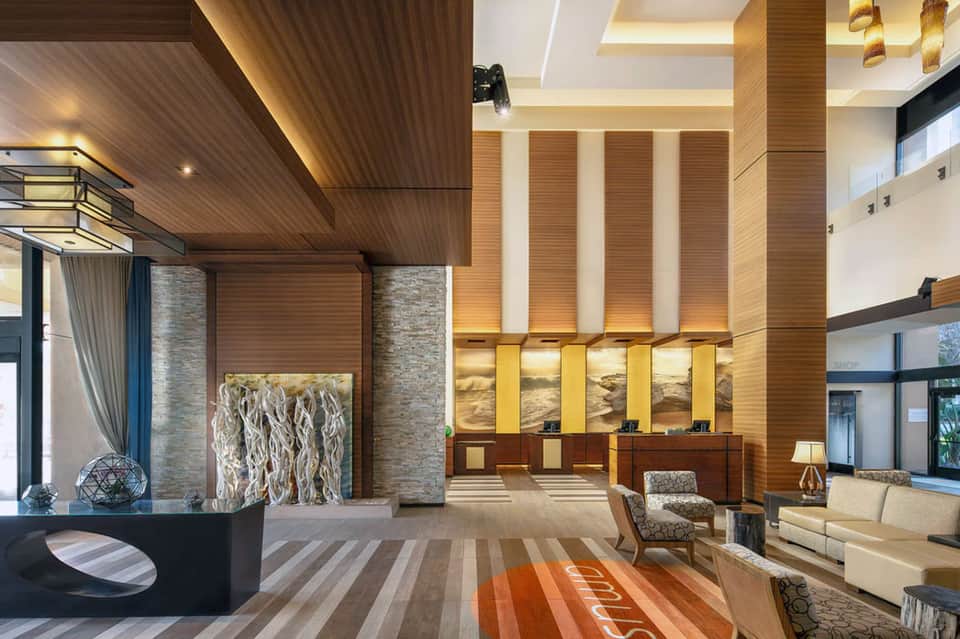 Modern hotel lobby featuring wooden accent walls, illuminated columns, reception desk, and contemporary furnishings