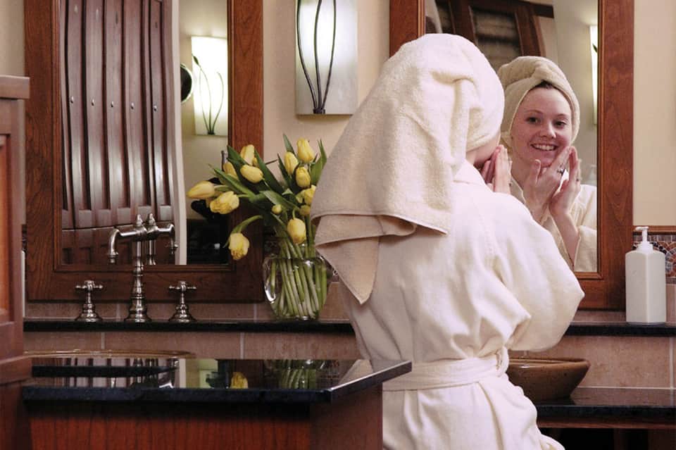 Spa bathroom with woman in white robe at sink with yellow flowers and mirrors