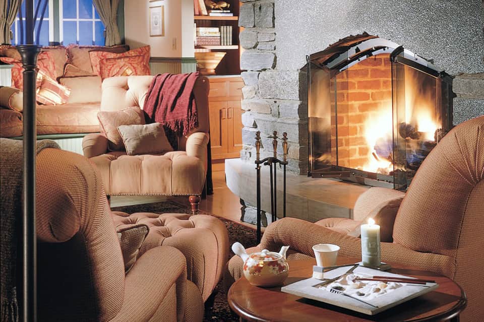 Cozy fireplace lounge with upholstered seating, warm lighting, and stone fireplace