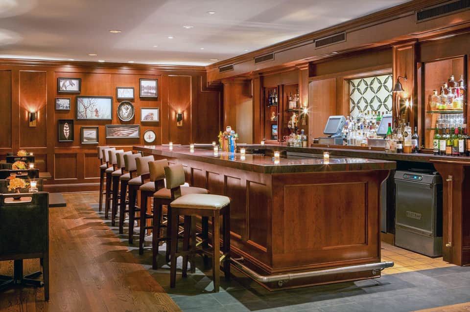 Elegant wood-paneled hotel bar with leather seating, extensive liquor selection, and warm lighting