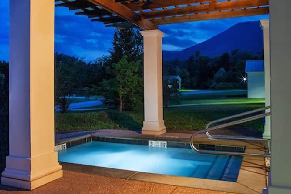 Illuminated spa pool at dusk with pergola, columns, and landscape lighting