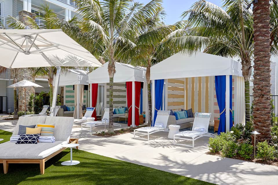 Multiple white cabanas with colorful curtains on manicured lawn with palm trees