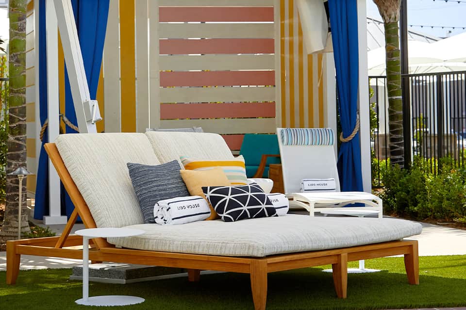 Outdoor daybed with canopy, colorful pillows, and blue curtains in cabana