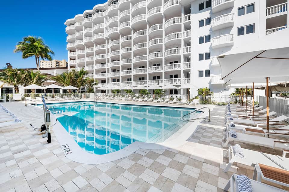 Resort swimming pool with lounge chairs, umbrellas, and white apartment building