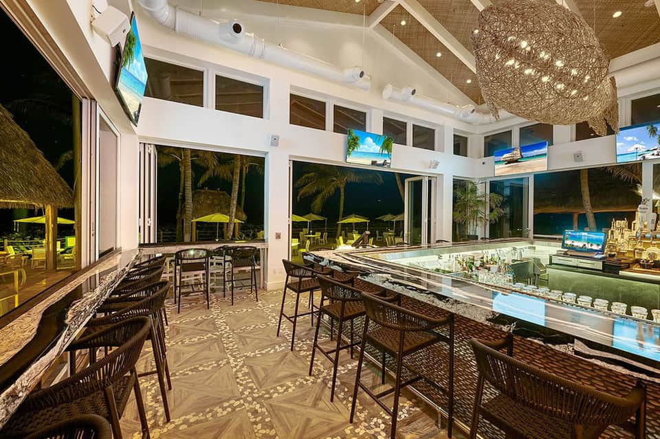 Modern beachfront bar with woven pendant light, glass counters, and ocean view at night