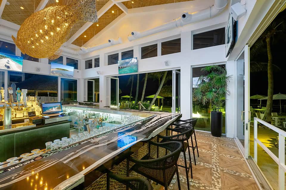 Contemporary bar with woven pendant light, extensive windows, and evening view of tropical landscape