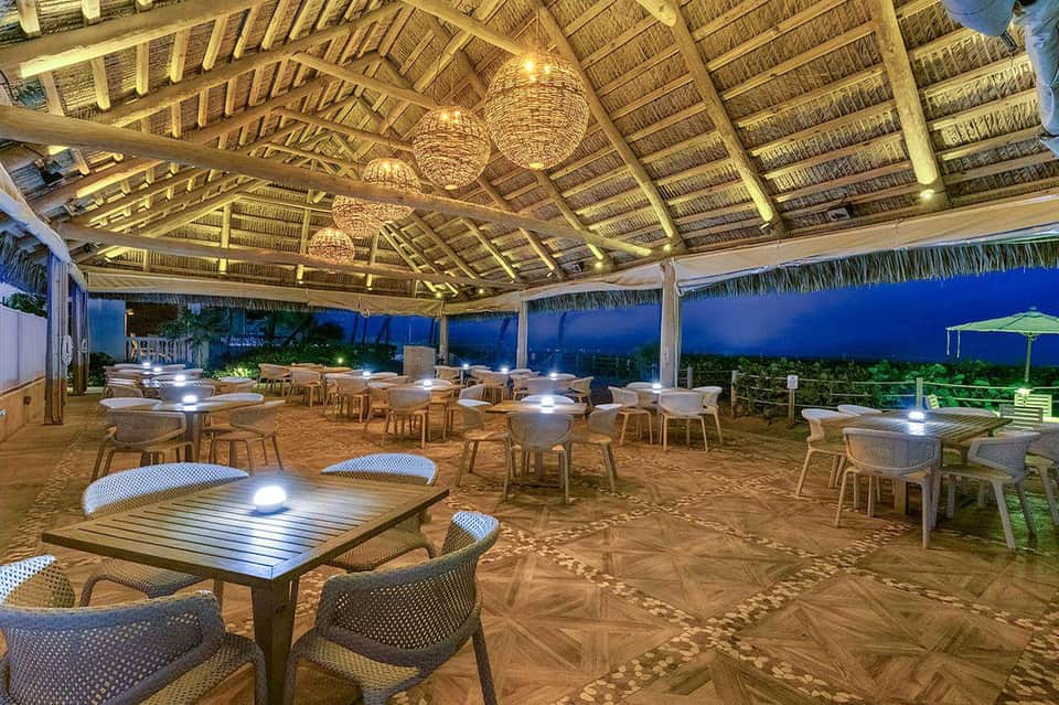 Covered beachfront dining area with woven ceiling, tables and chairs at twilight with ocean view
