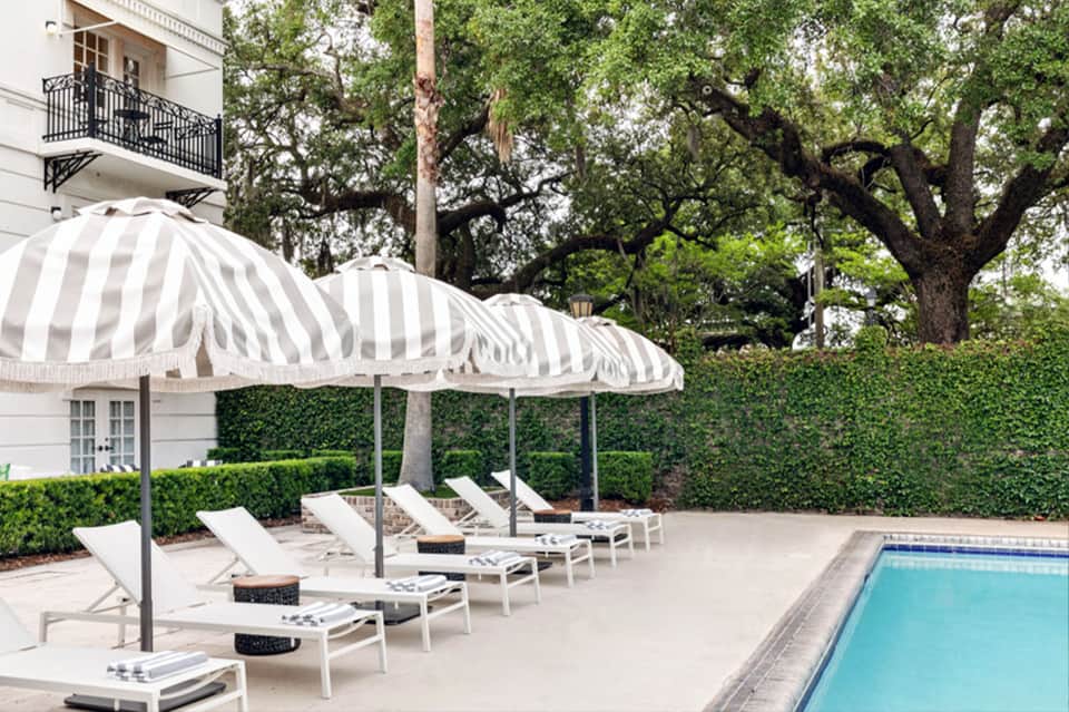 Elegant poolside seating with white loungers, striped umbrellas, and manicured hedge backdrop