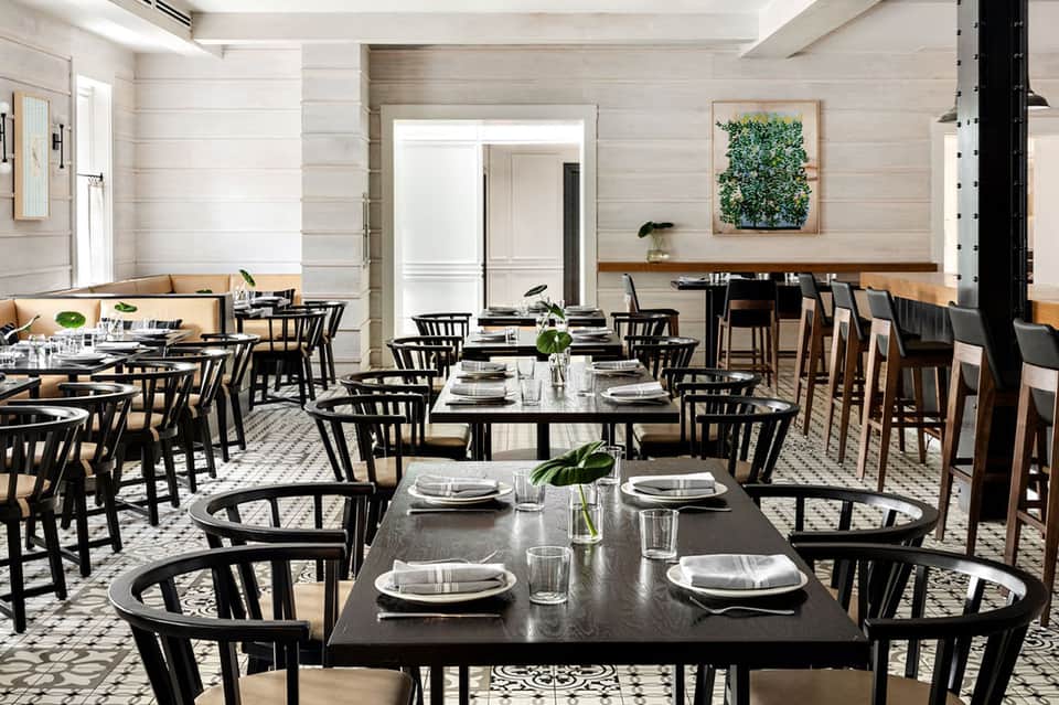 Fine dining restaurant with black chairs, long tables, white linens, and modern minimalist design
