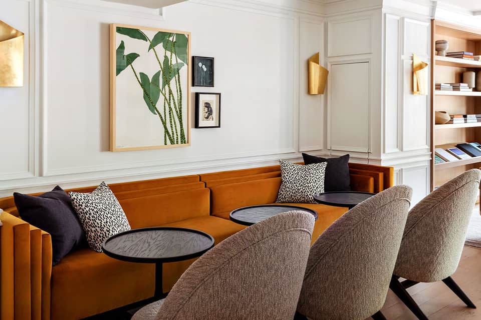 Modern lobby lounge with orange curved sofa, neutral chairs, gold sconces, and botanical art