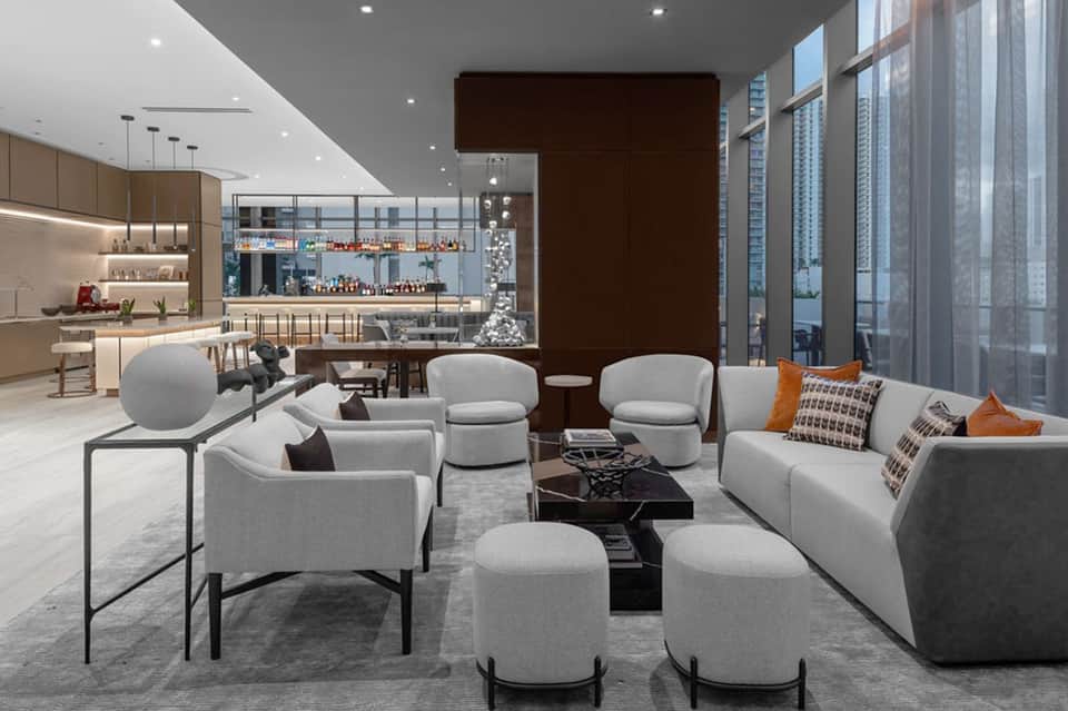 Contemporary high-rise hotel lounge with gray furniture, bar view, kitchen, and city skyline windows