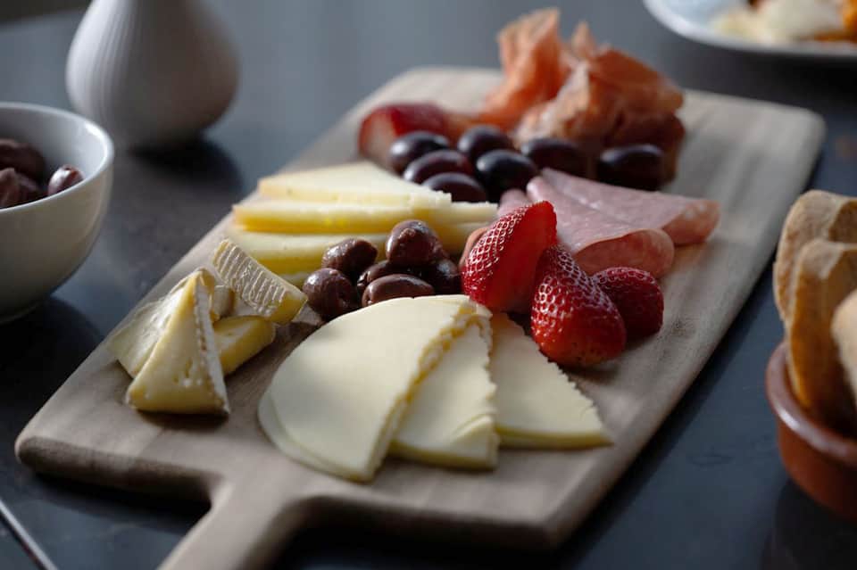 Charcuterie board with assorted cheeses, cured meats, berries, and olives on marble surface