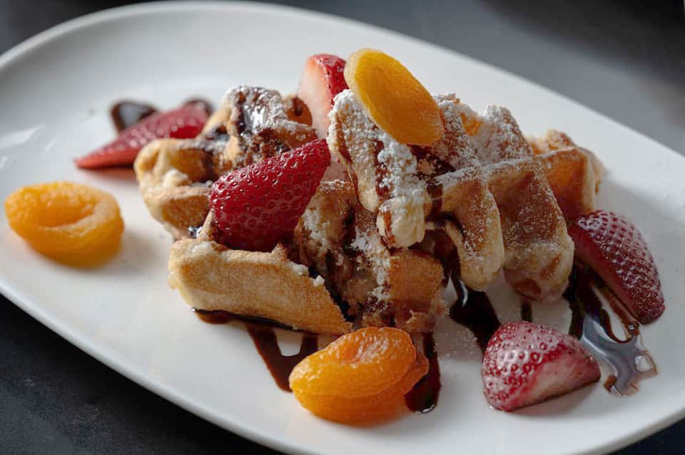 Elegant waffle dessert plated with fresh strawberries, apricots, and powdered sugar