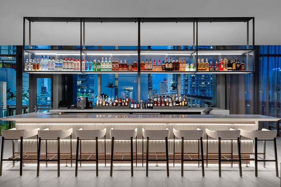 Upscale bar with extensive spirit collection, white bar seating, and city window views