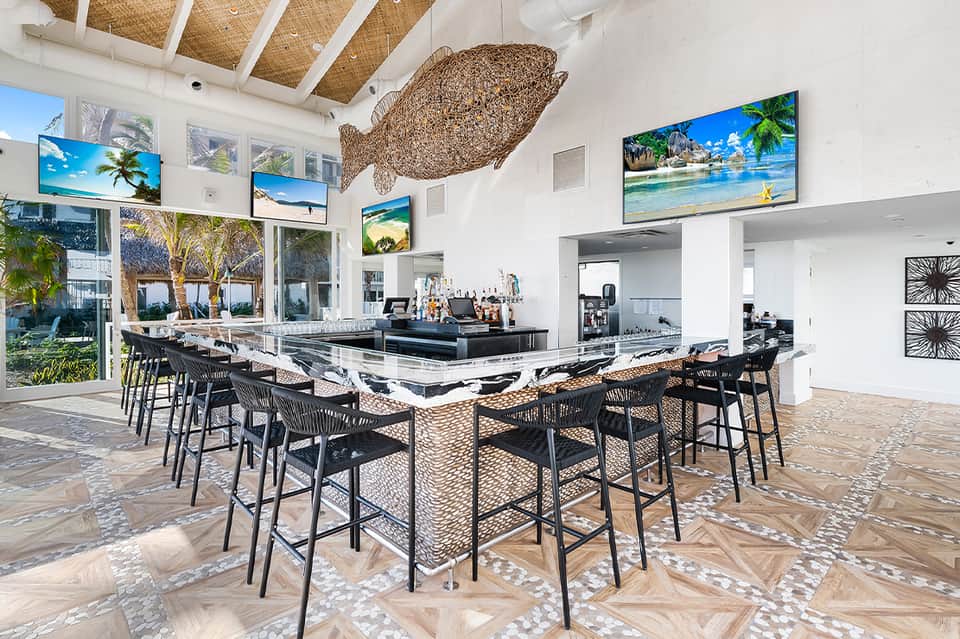 Contemporary beach club bar with modern furniture, large windows, and tropical decor