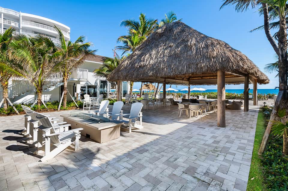 Beachfront deck with tiki bar, fire pit, and white lounge chairs overlooking ocean