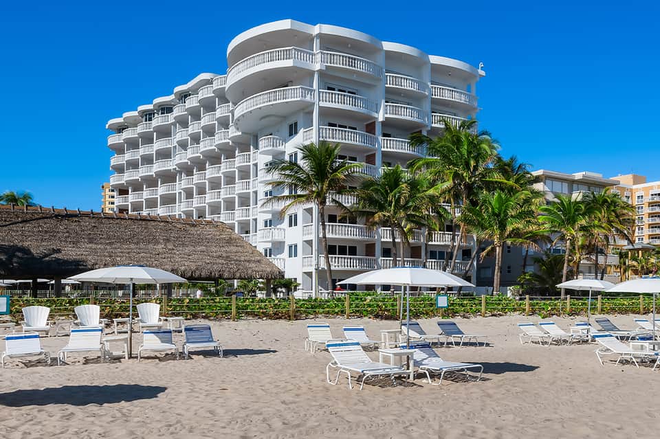Contemporary beachfront resort building with curved balconies, palm trees, and lounge area